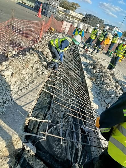 JCL workers reinforcing a concrete drainage channel with rebar on an industrial site