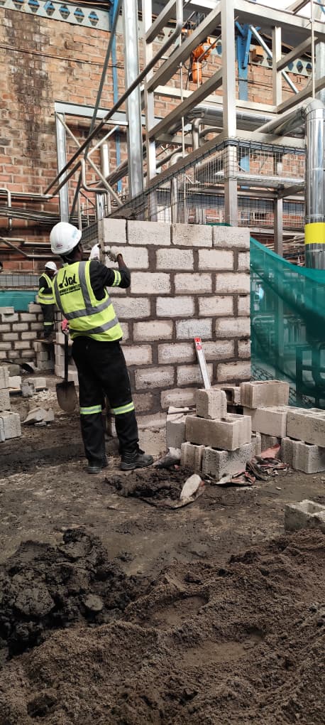 JCL mason building a blockwork wall on an industrial site beneath overhead steel gantries