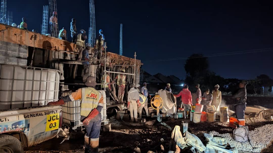 JCL crew conducting a night concrete pour with mixers, scaffolding and branded supply trailer