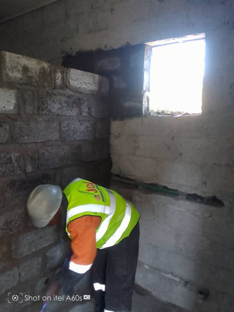 JCL worker in branded vest plastering an interior blockwork wall