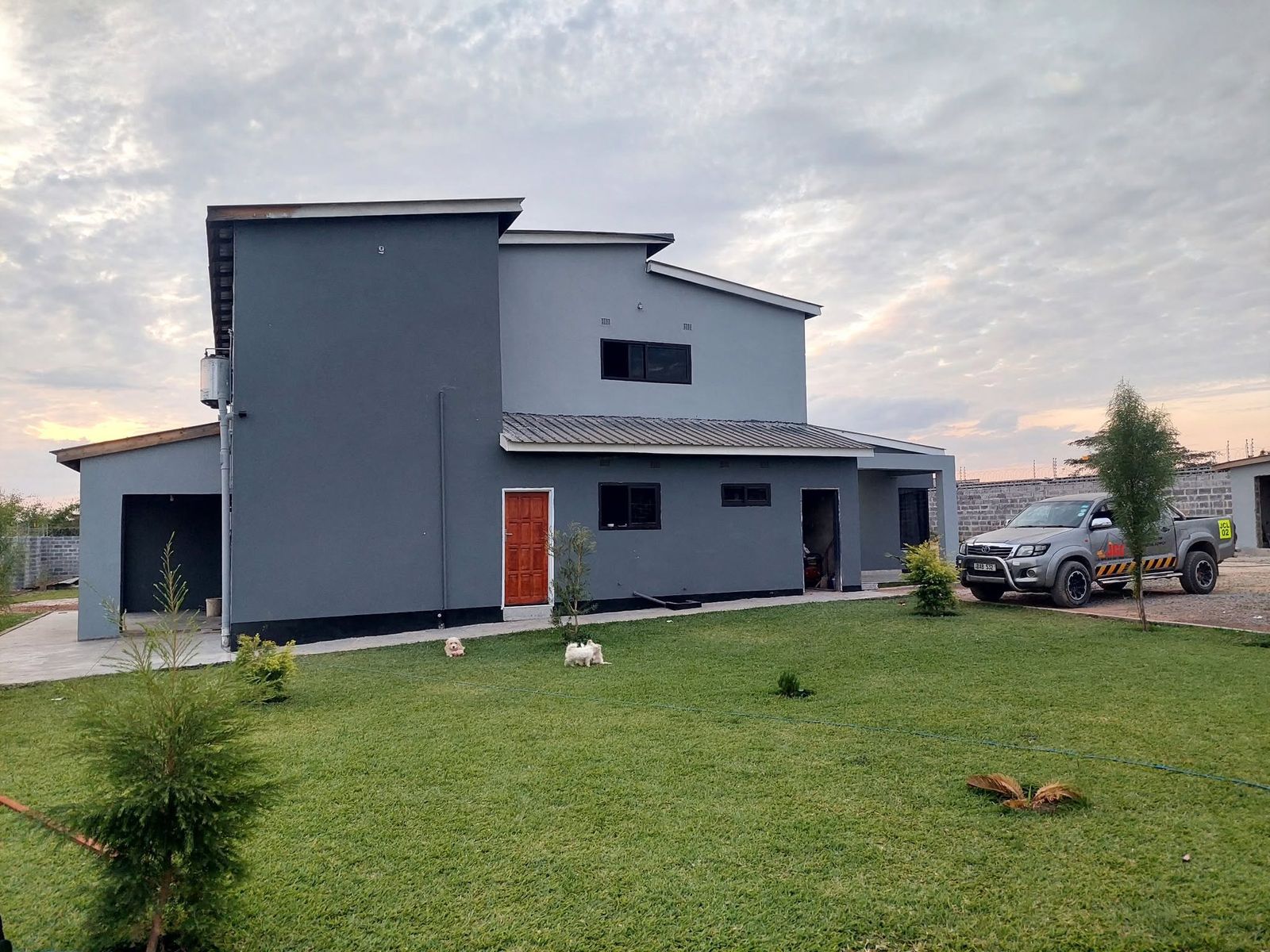 Finished contemporary grey double-storey house with green lawn and company vehicle