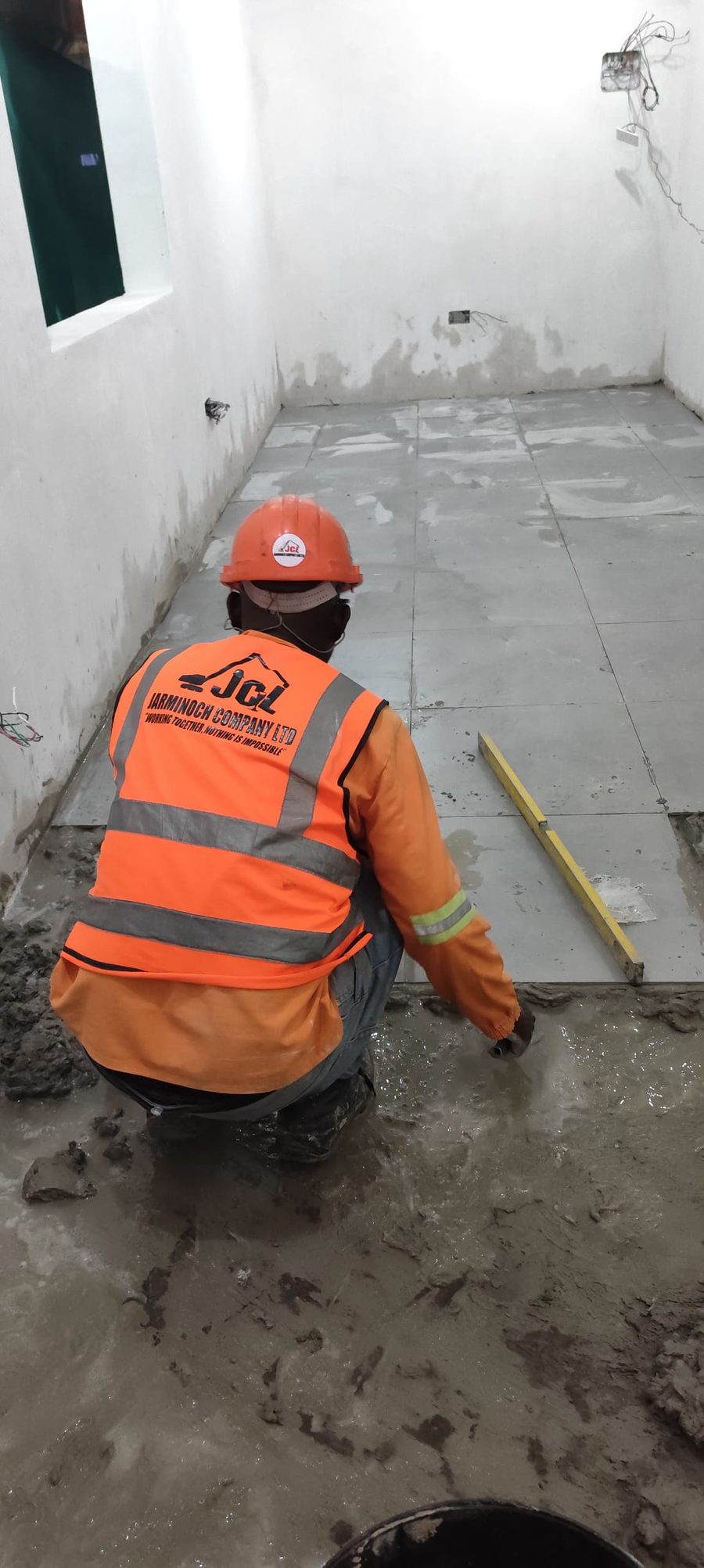 JCL tiler in branded orange vest laying large porcelain floor tiles