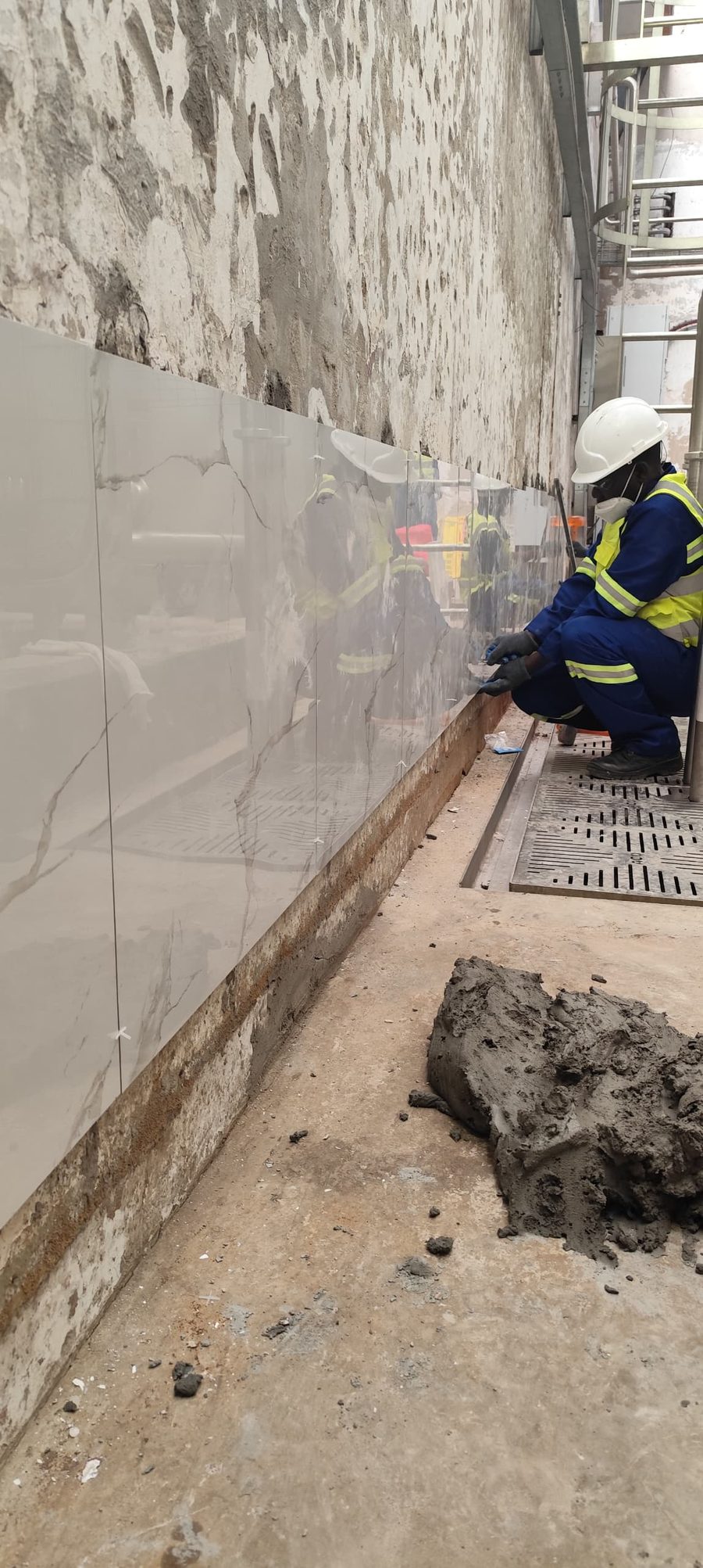 Worker in white helmet fixing large marble-effect wall tiles in full PPE